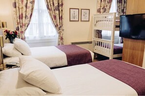 A hotel room with two beds, a bunk bed, a TV, and a window with curtains. - Athena (London)