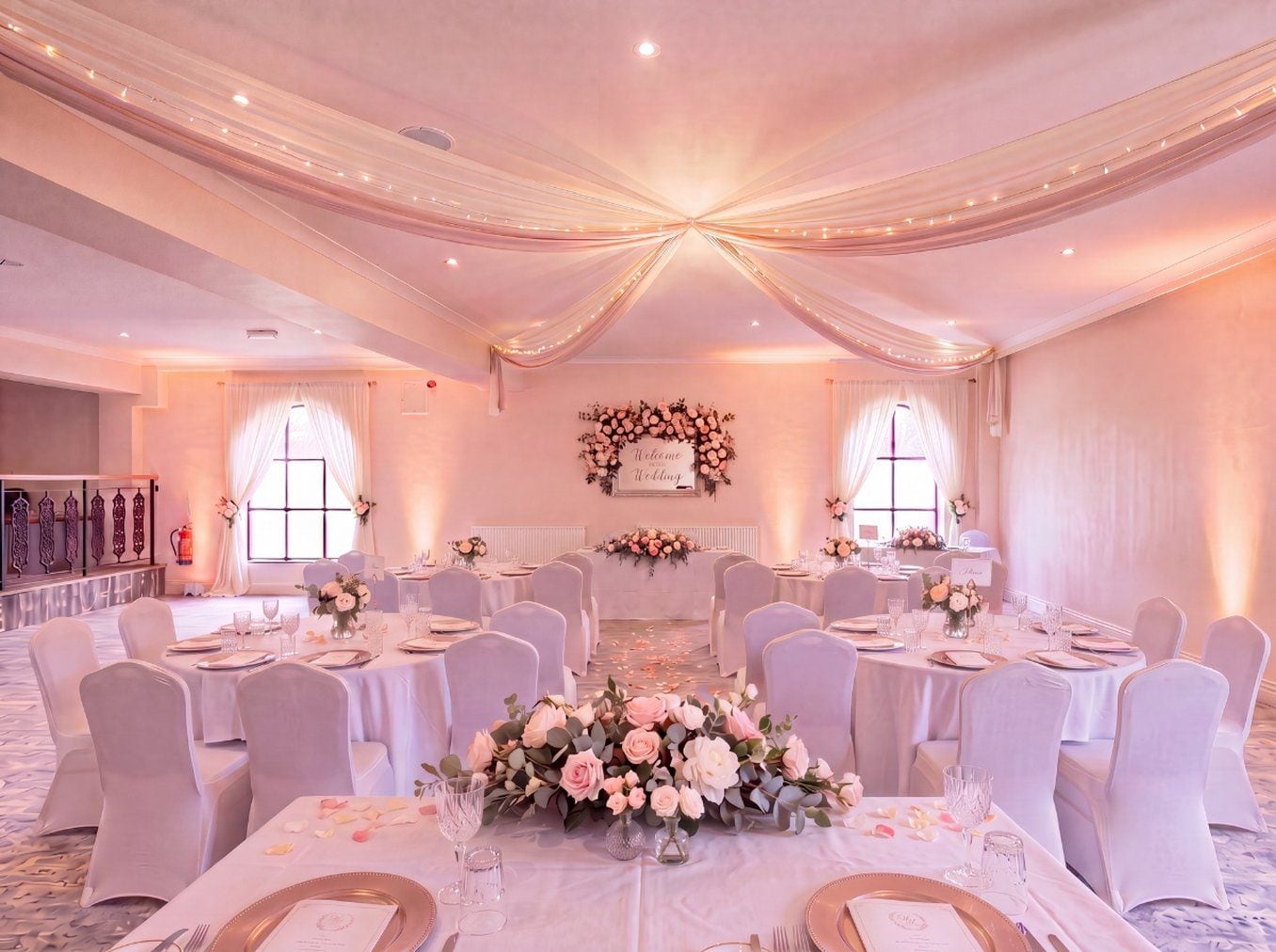 A banquet hall with round tables, white tablecloths, and floral centerpieces.