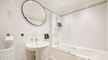 Un baño con un lavabo blanco, un espejo redondo, una ducha con cerramiento de vidrio y una bañera blanca.
