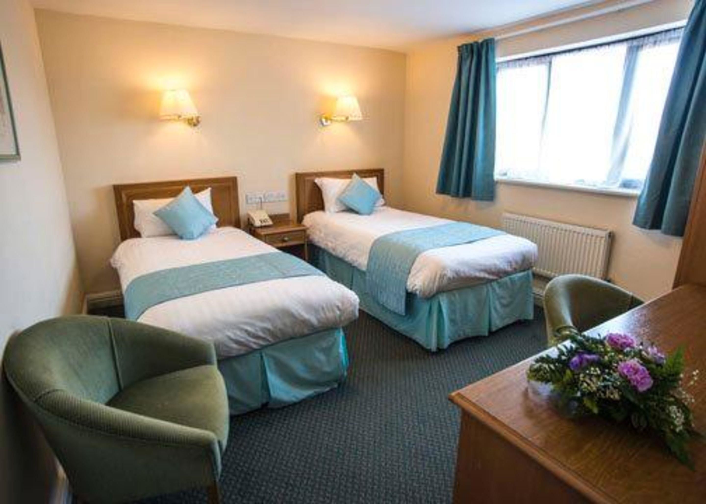 A hotel room with two beds, a desk, a chair, and a window with curtains.