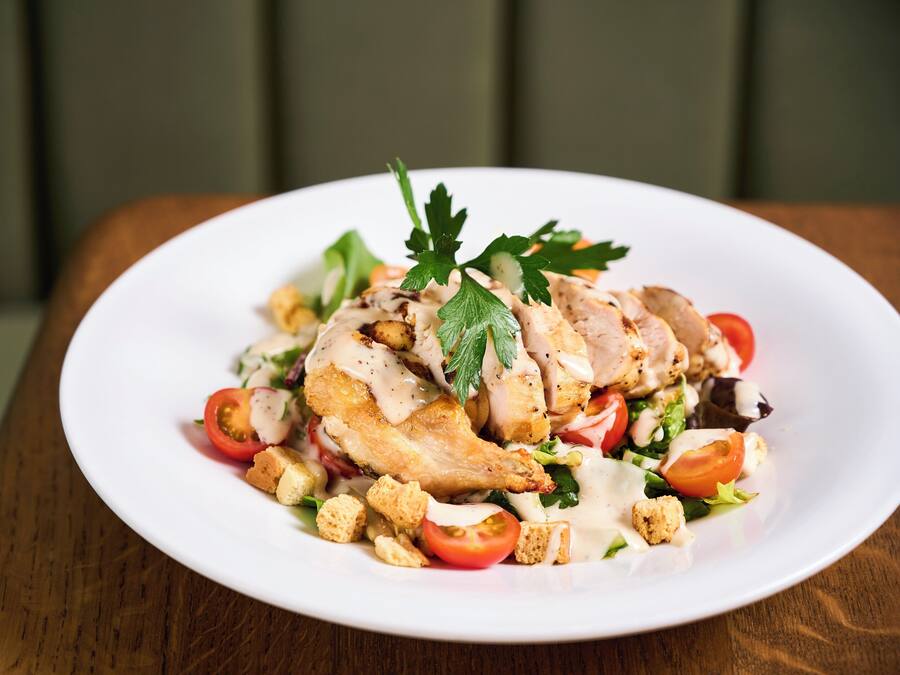 Een witte schaal met een salade met kip, tomaten en croutons.