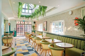 A restaurant with green booths, wooden tables, and hanging plants. - Garner Hotel Birmingham South East by IHG (Birmingham)