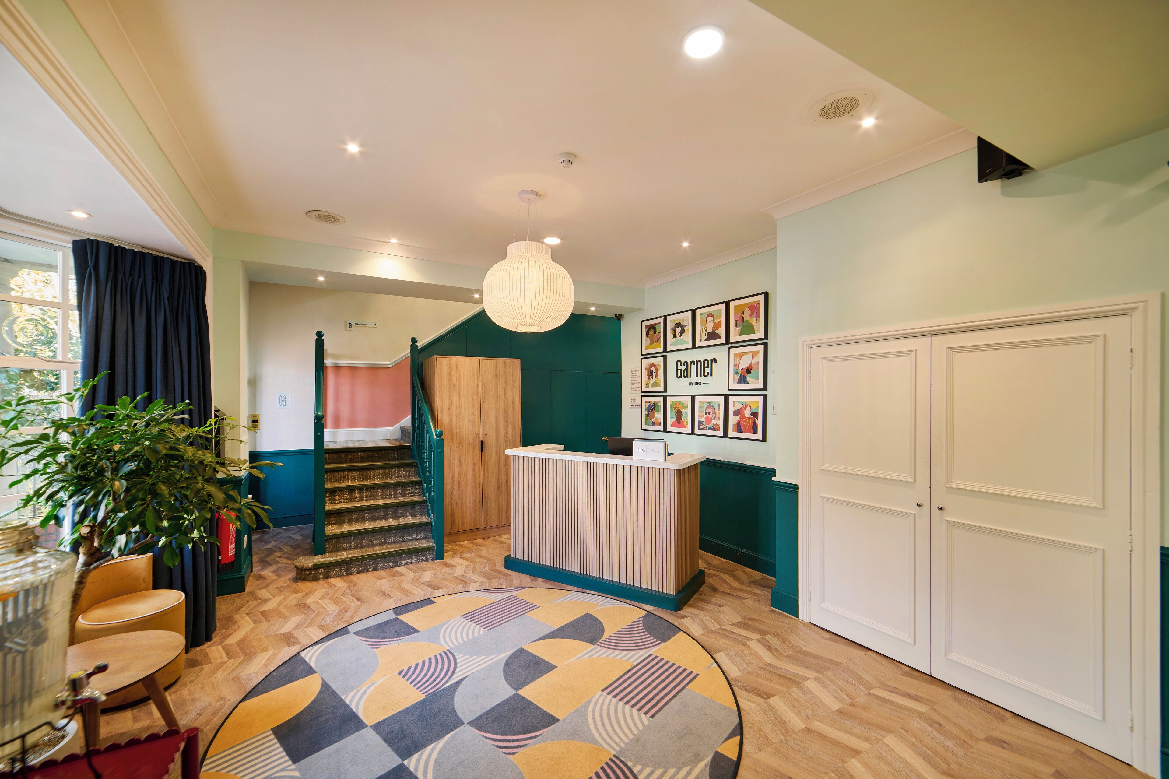 A hotel lobby with a reception desk, a staircase, and a patterned rug.