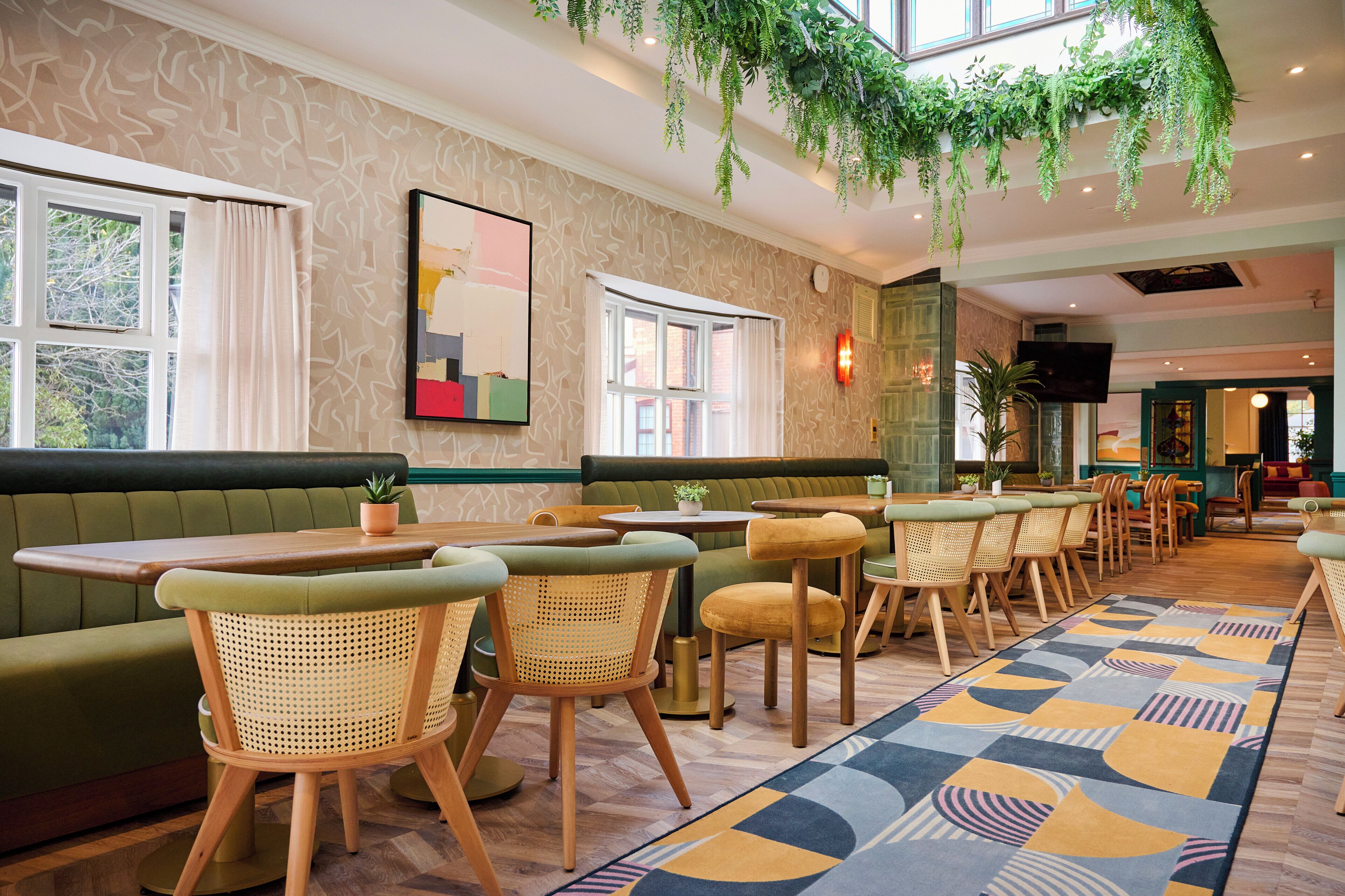 Un restaurante con asientos de tapicería verde, mesas de madera y sillas de mimbre.