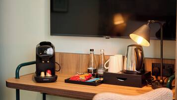 A wooden desk with a Philips coffee maker, a kettle, a lamp, and a tray with snacks.