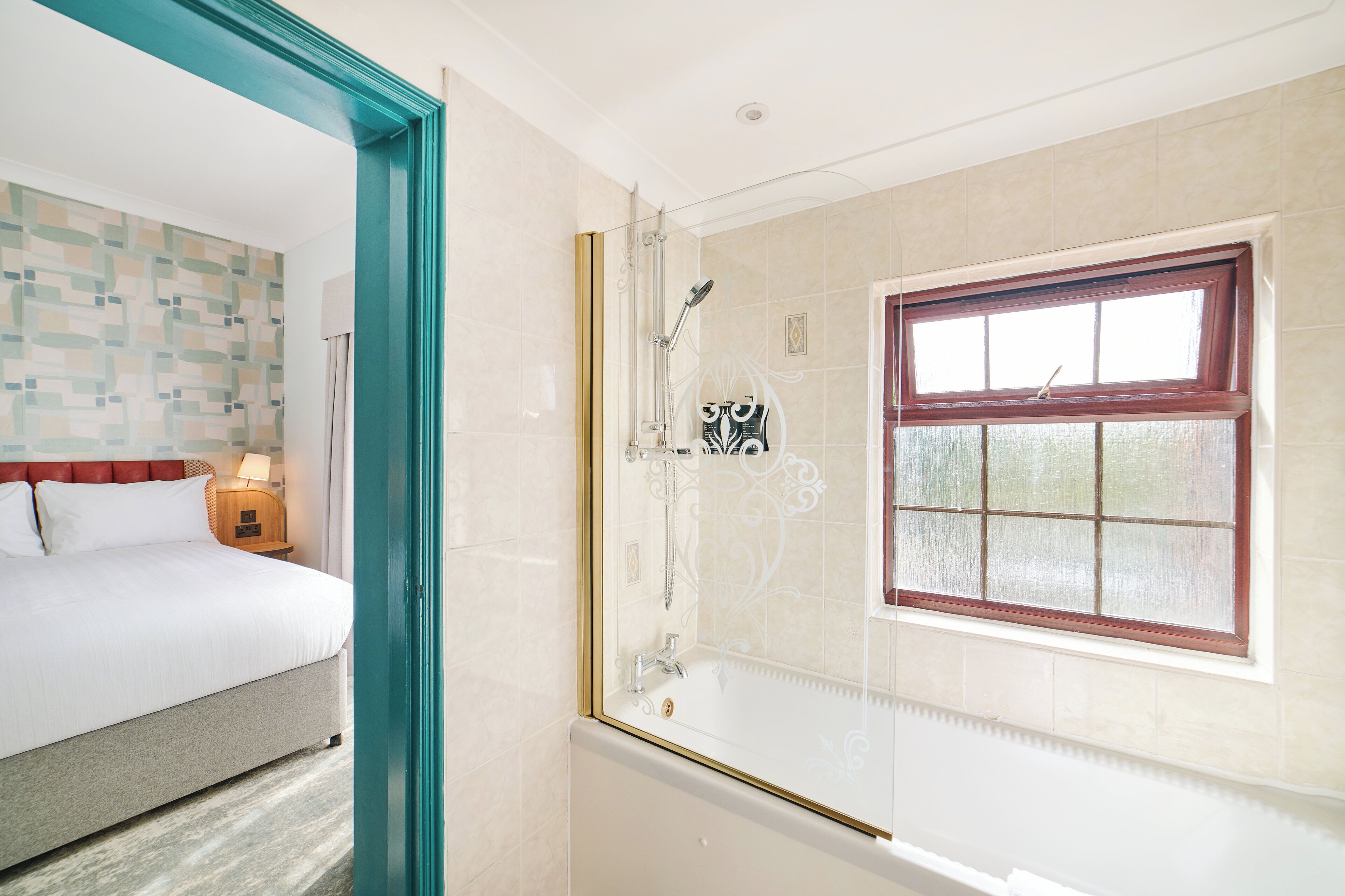 A hotel room with a bed, a shower area with a glass door, and a window with a view.