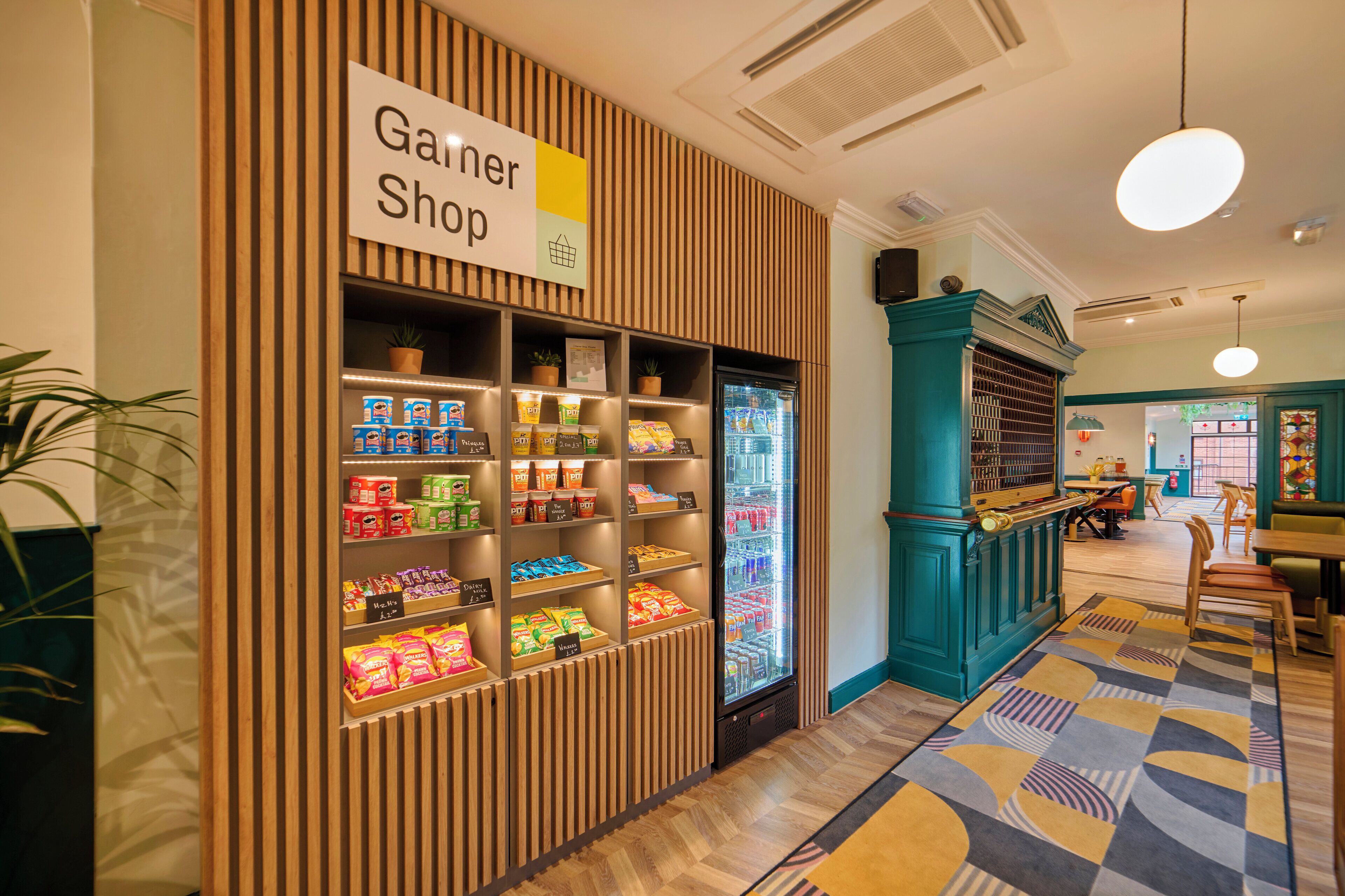 Una tienda llamada 'Ganer Shop' con estantes llenos de refrigerios y un refrigerador expositor.