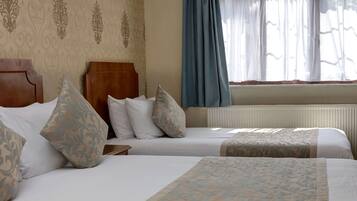 A hotel room with two beds, a wooden headboard, patterned pillows, and a window with blue curtains.