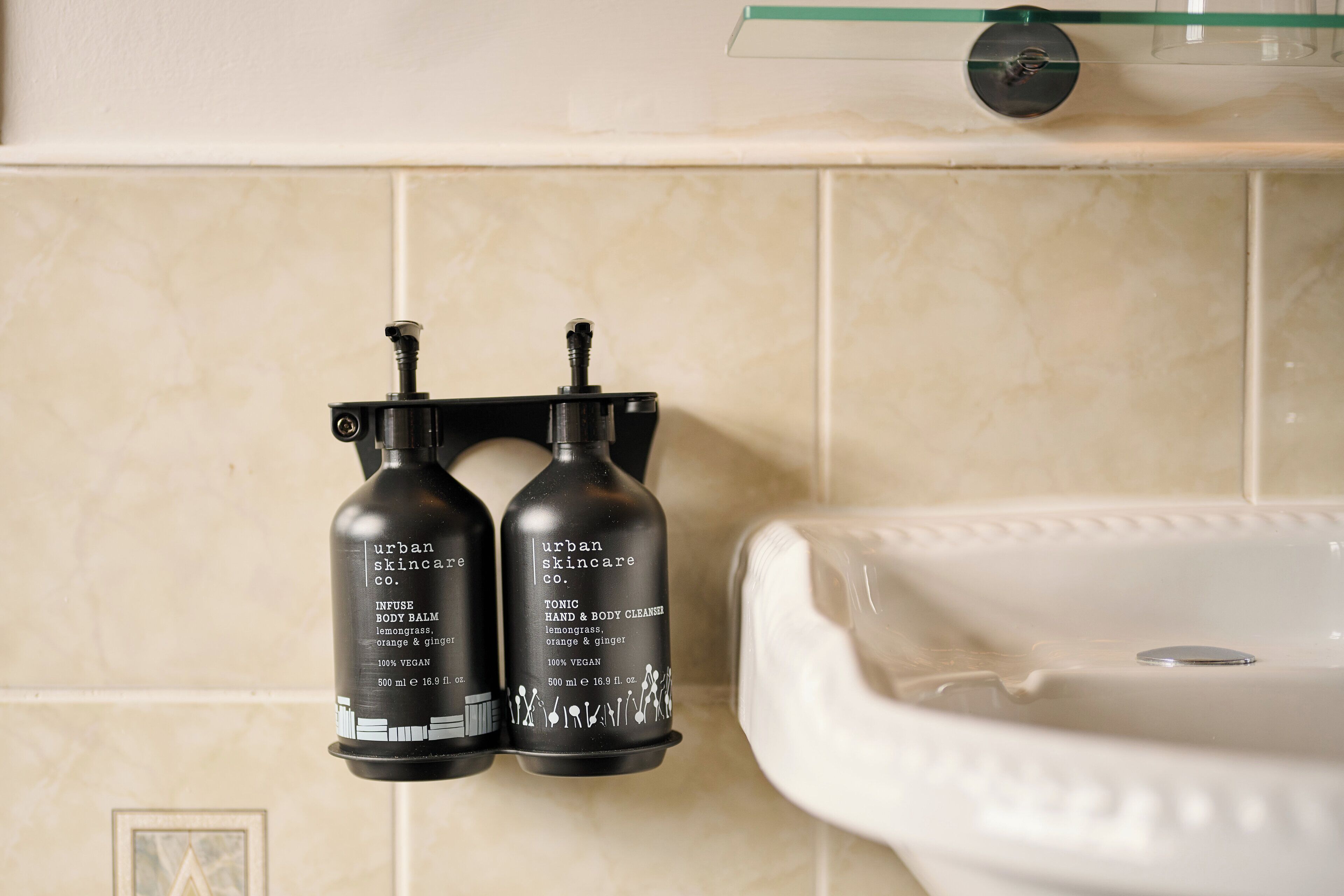 Two black bottles of Urban Skincare products mounted on a wall next to a white sink.