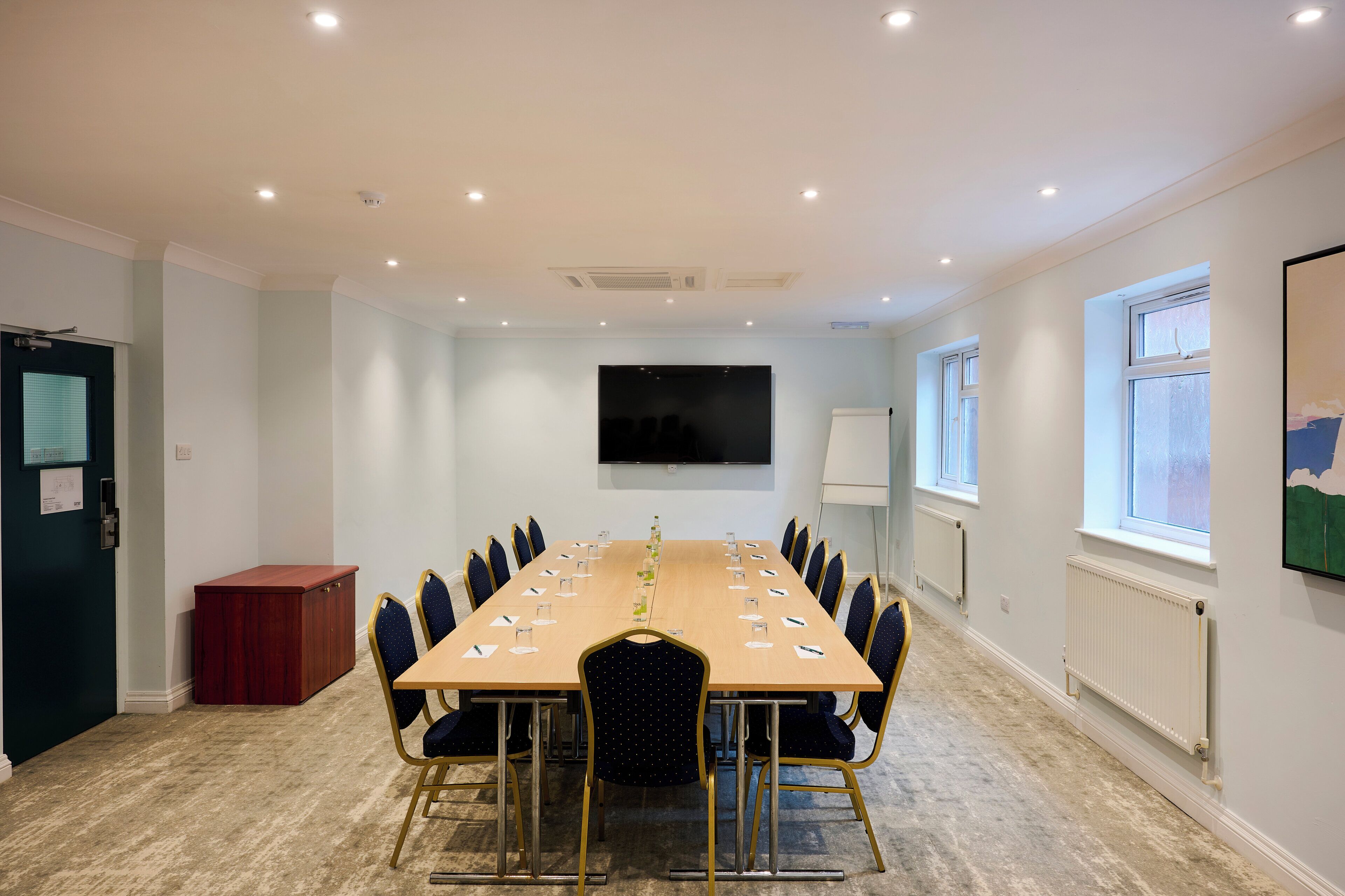 A conference room with a long table, chairs, a projector screen, and a window.