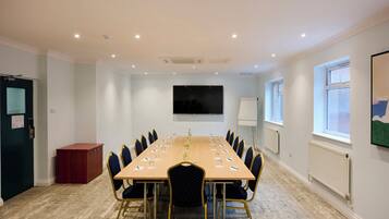 A conference room with a long table, chairs, a projector screen, and a window.