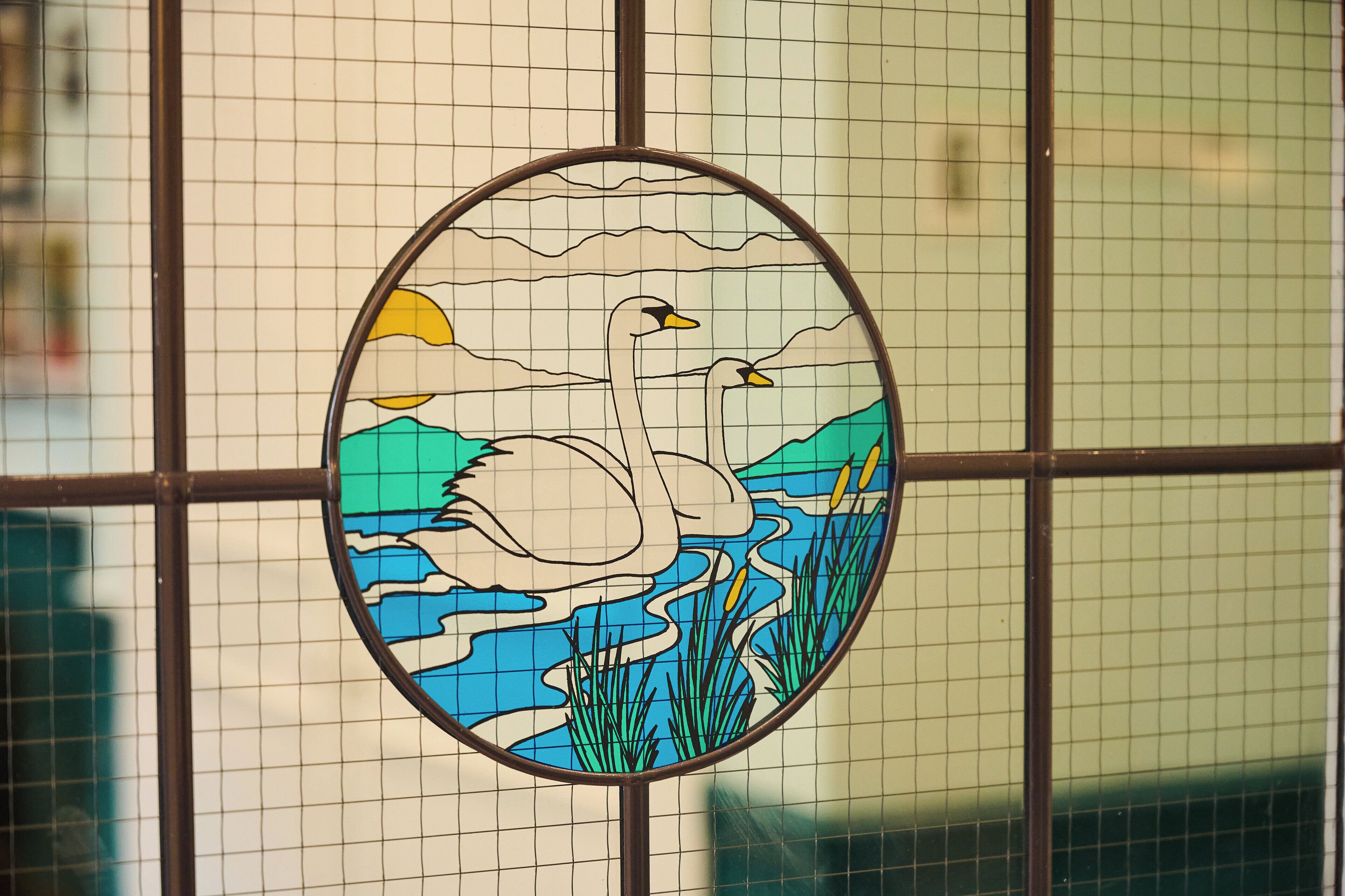 Une vitre décorée avec des motifs en vitrail représentant un cygne et un paysage.