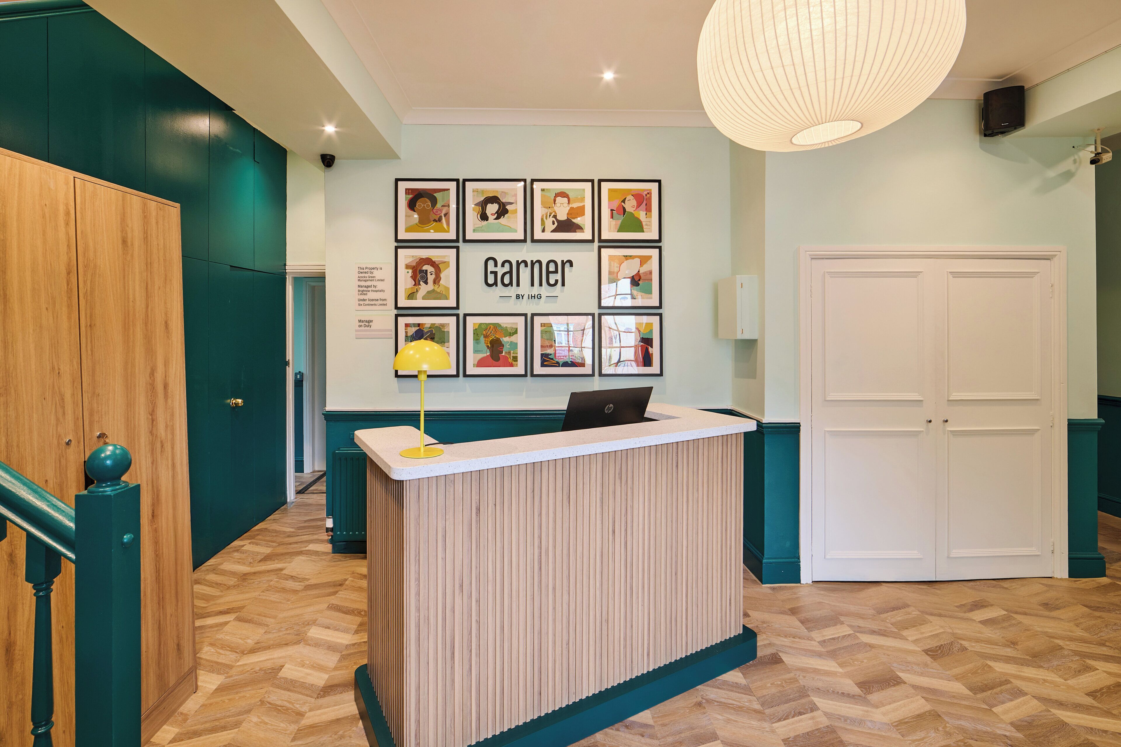 Un comptoir d’accueil avec un ordinateur portable, des œuvres d’art encadrées accrochées au mur et une porte sur la droite.
