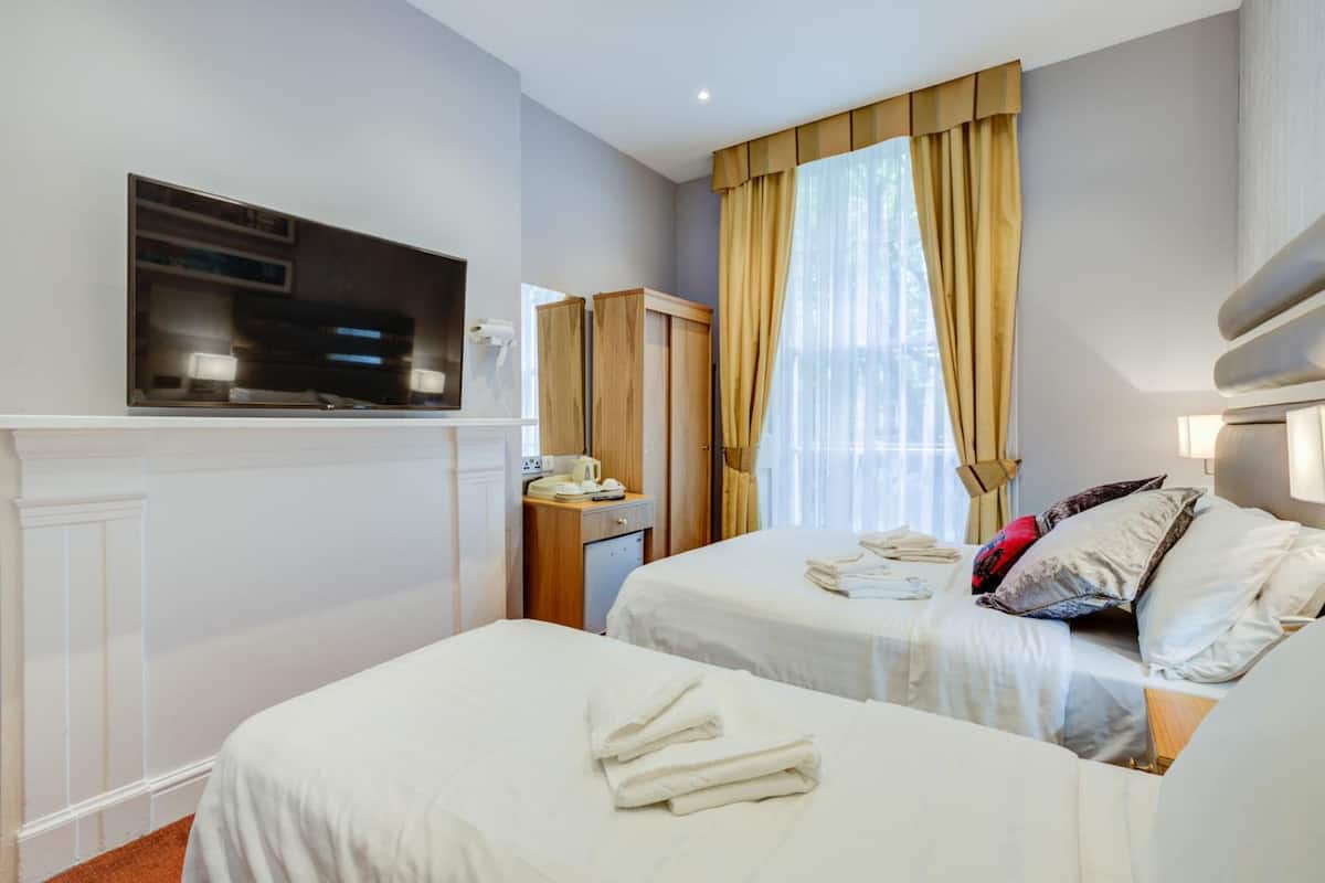 Una habitación de hotel con dos camas, televisión, escritorio con teléfono y ventana con cortinas.