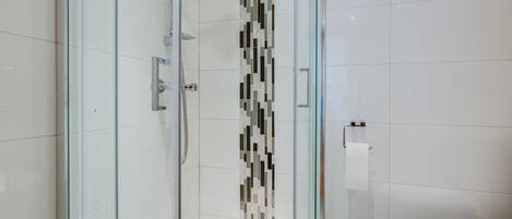 A modern bathroom with a glass-enclosed shower, a tiled wall with a decorative pattern, and a white toilet.
