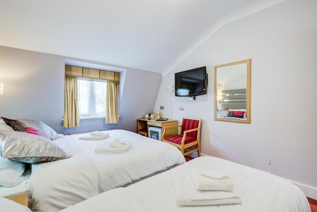 Habitación de hotel con dos camas, un escritorio, una silla, un televisor y un espejo en la pared.