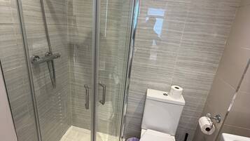 A modern bathroom with a glass-enclosed shower, a toilet, and a sink.