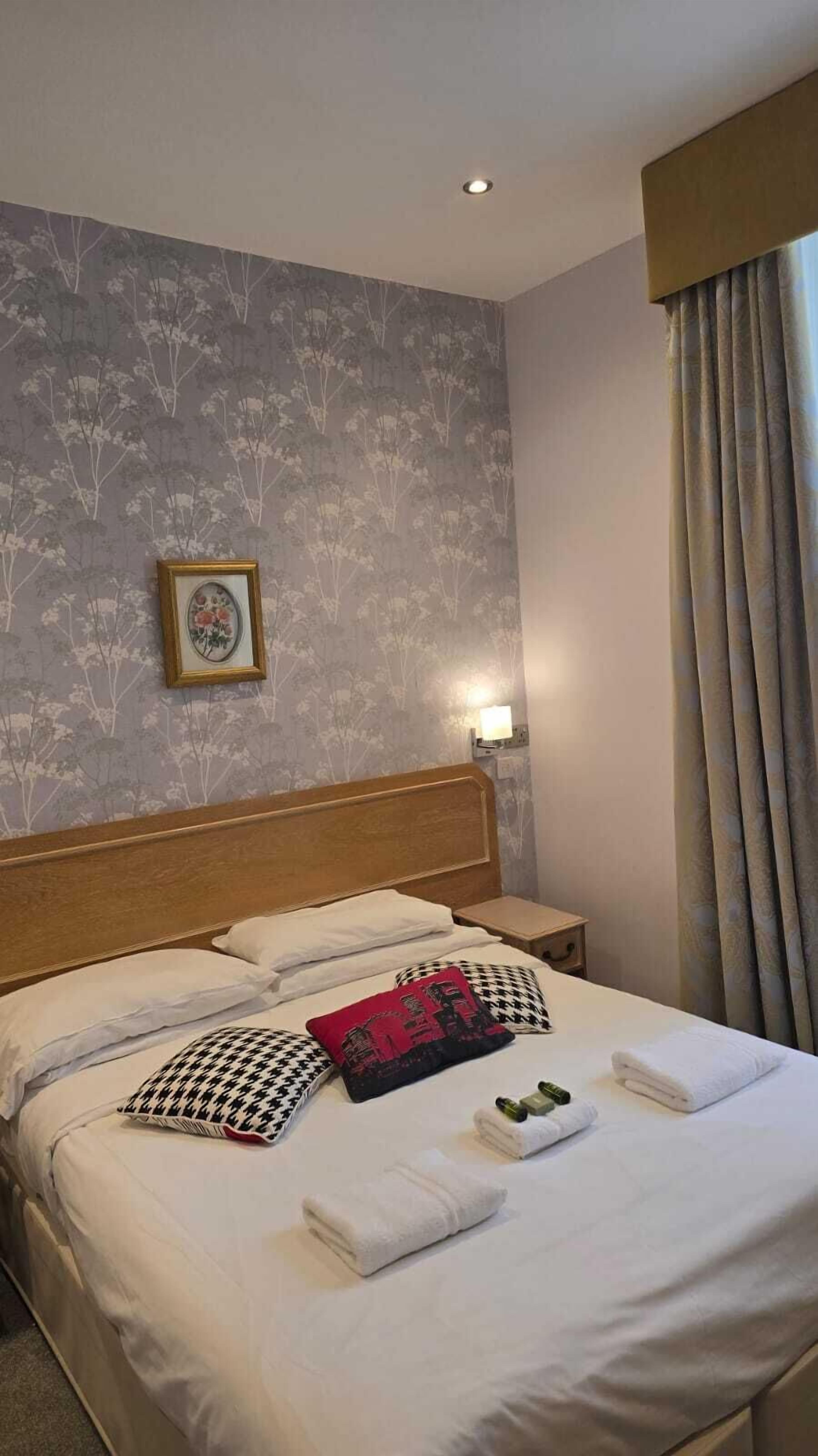 A hotel room with a neatly made bed, a framed picture on the wall, and a nightstand with a lamp.