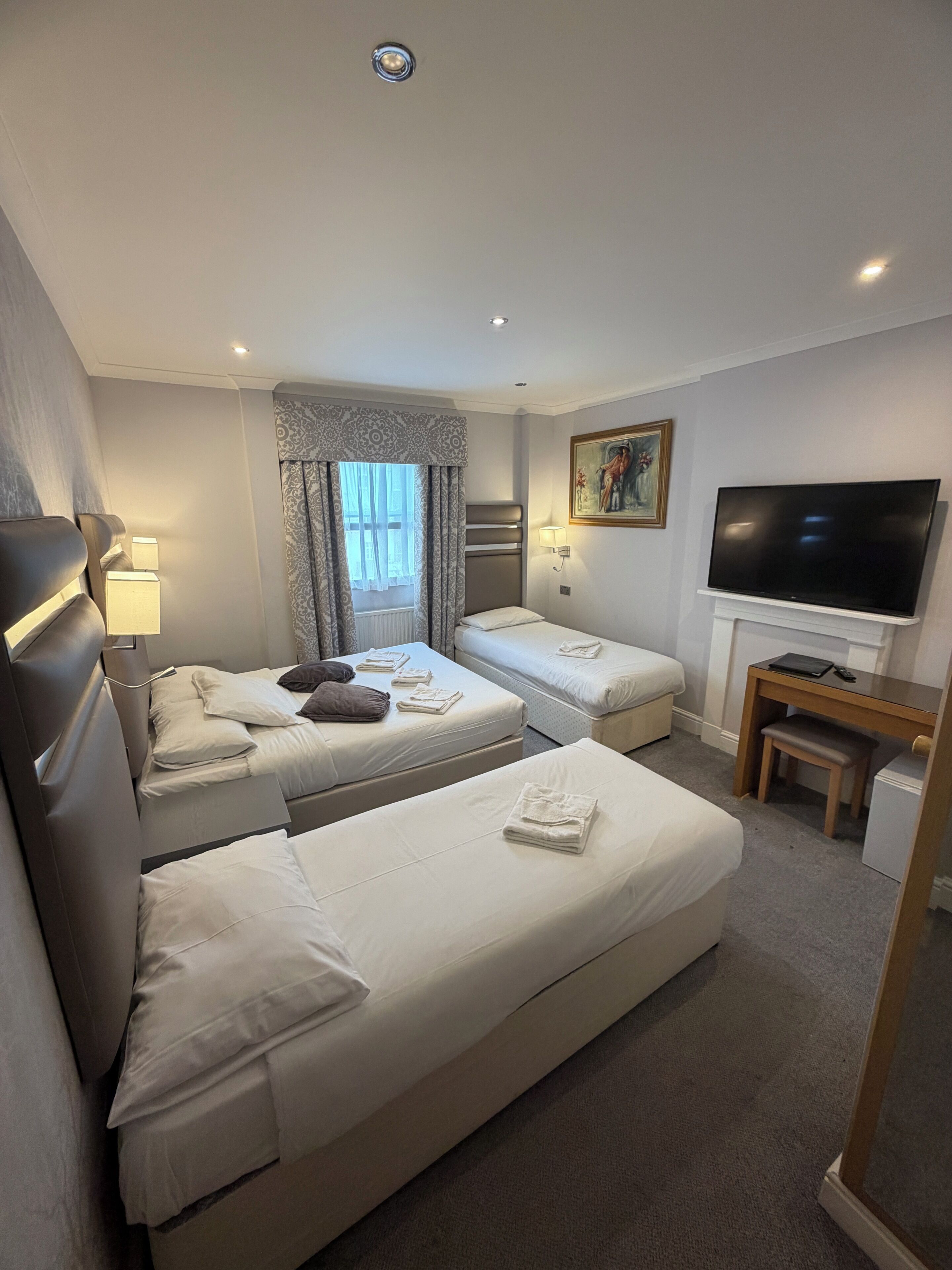 A hotel room with two beds, a TV, a desk, and a window with curtains.