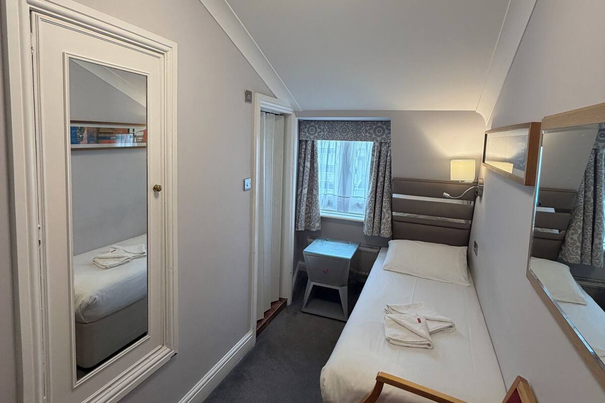 Una habitación de hotel con cama, escritorio, silla, armario y espejo.