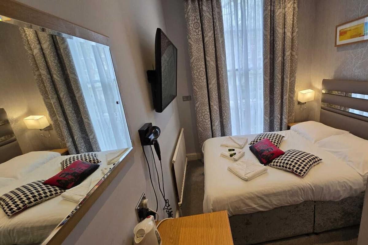 Habitación de hotel con dos camas, un espejo, un televisor y una mesita de noche con lámpara.