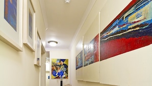 Ein Flur mit rotem Teppich, weißen Wänden und Kunstwerken. Eine Wand ist mit einem Stuhl und einem Heizkörper versehen.