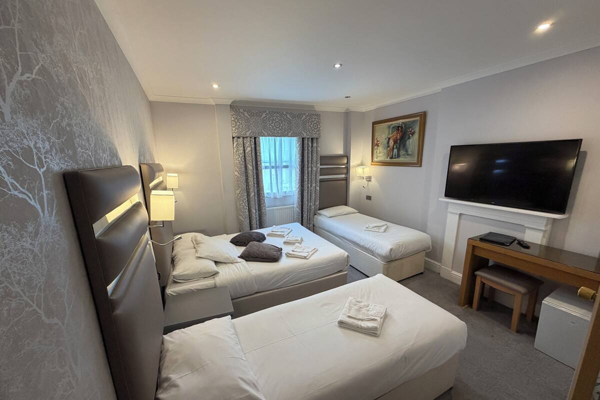 Habitación de hotel con dos camas, televisión, escritorio y un refrigerador pequeño.