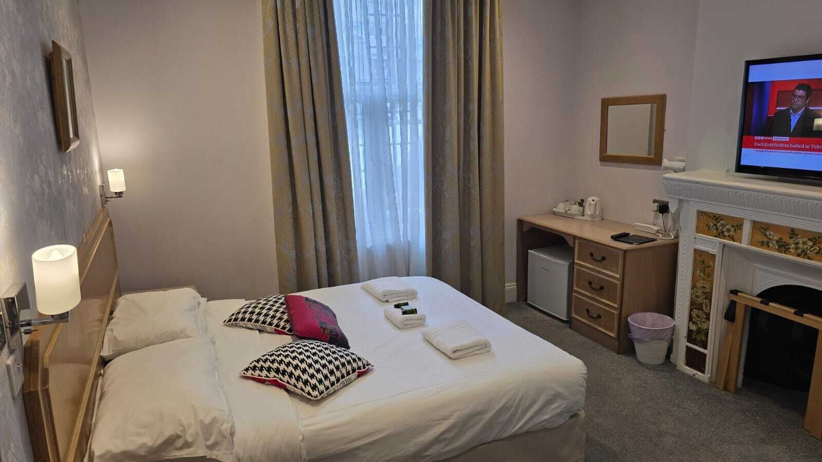 A hotel room with a bed, a desk, a television, a fireplace, and a window with curtains.