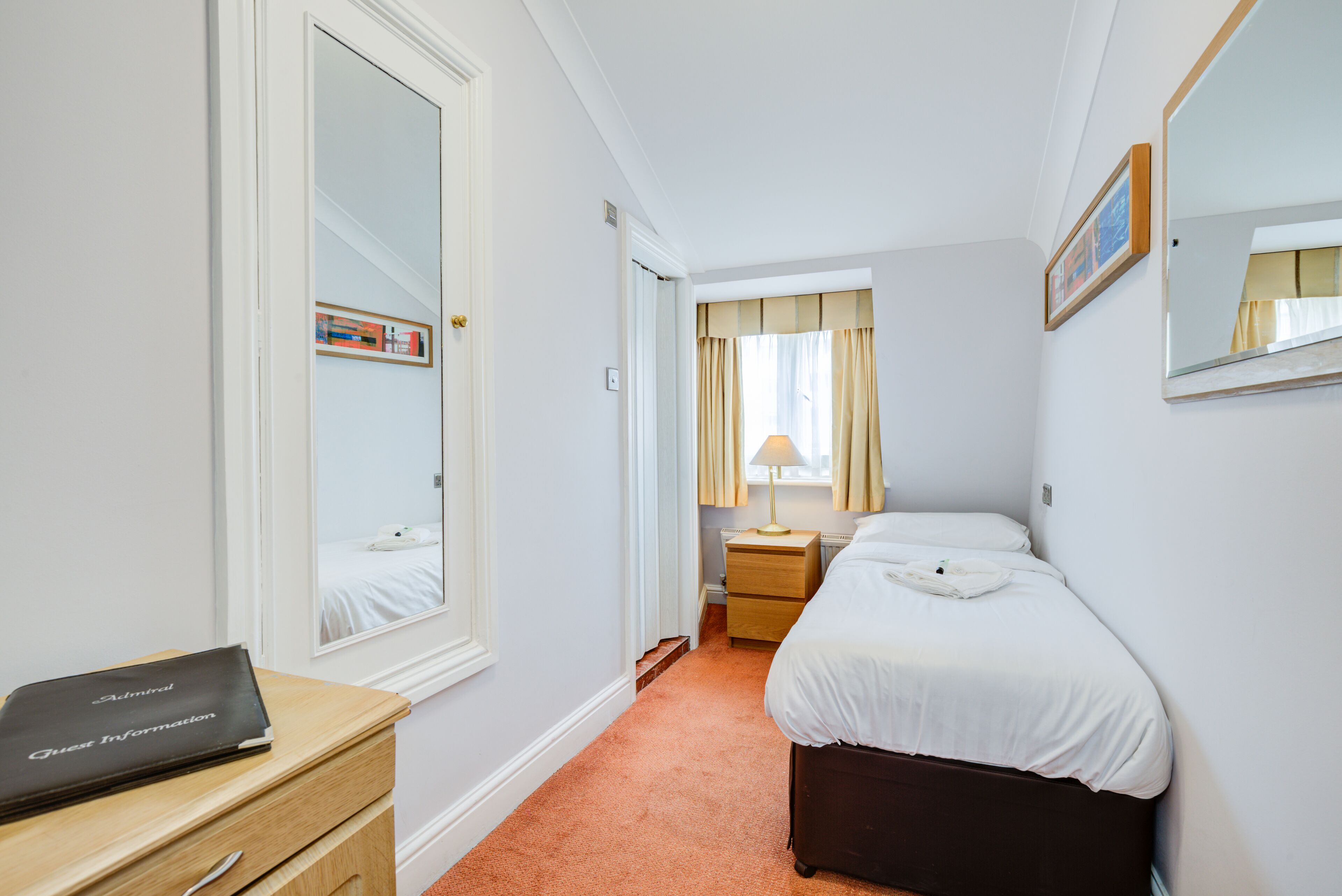 Ein Hotelzimmer mit Bett, Schreibtisch mit Laptop, Nachttisch und einem Fenster mit Vorhängen.