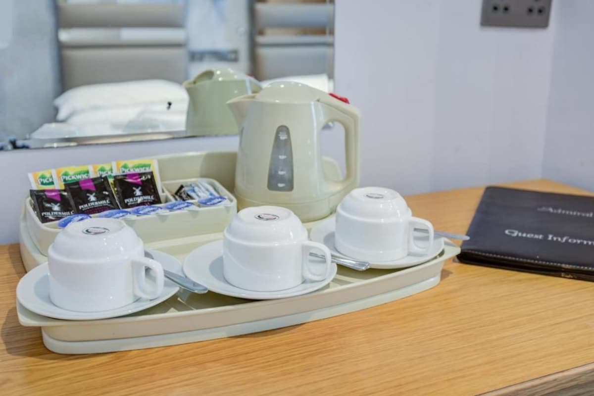 A tray with white cups and saucers, a teapot, and packets of pick-me-up tea on a hotel table.