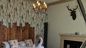 Une chambre à coucher avec un grand lit, un lustre, une cheminée et une tête de cerf décorative accrochée au mur.