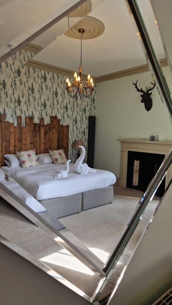 Un dormitorio con una cama grande, una araña de techo, una chimenea y una decoración de cabeza de ciervo en la pared.
