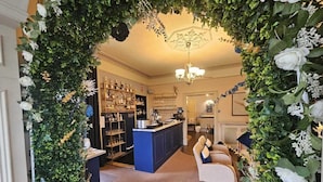 Un espace bar avec un comptoir bleu, des étagères remplies de bouteilles et un coin salon avec des chaises et une table.
