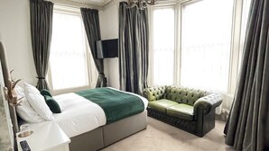 A bedroom with a bed, a sofa, a TV, and large windows with curtains.