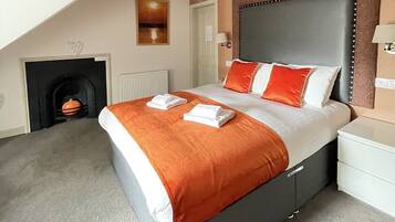 A modern bedroom with a large bed, a fireplace, and a sloped ceiling.