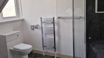 Un baño moderno con cabina de ducha de vidrio, inodoro blanco, lavamanos y ventana que proporciona luz natural.