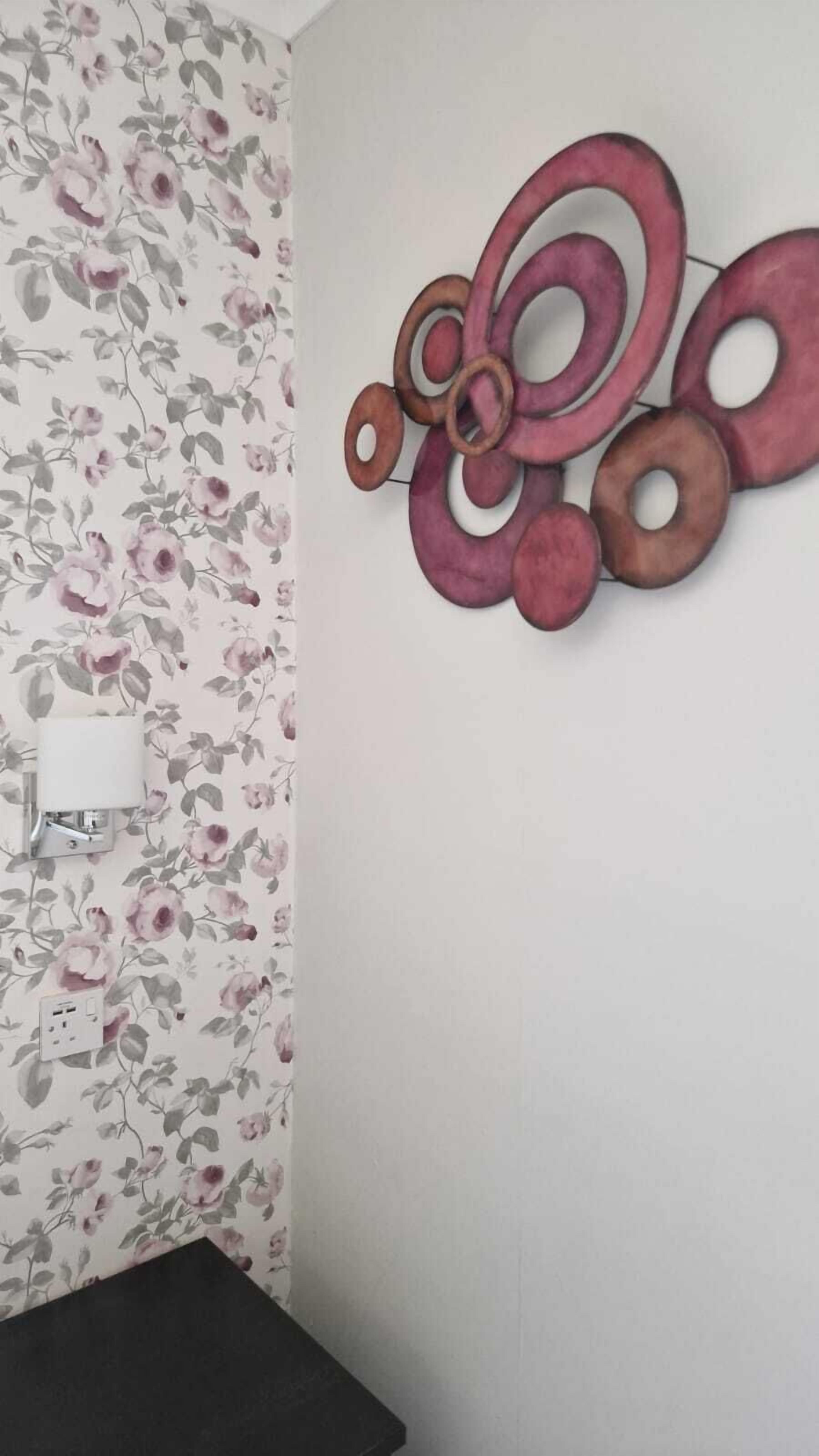 A bathroom with floral wallpaper, a wall-mounted light, and a black bench.