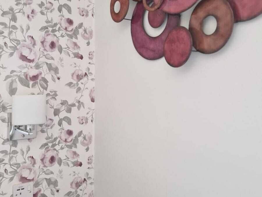 A bathroom with floral wallpaper, a wall-mounted light, and a black bench.