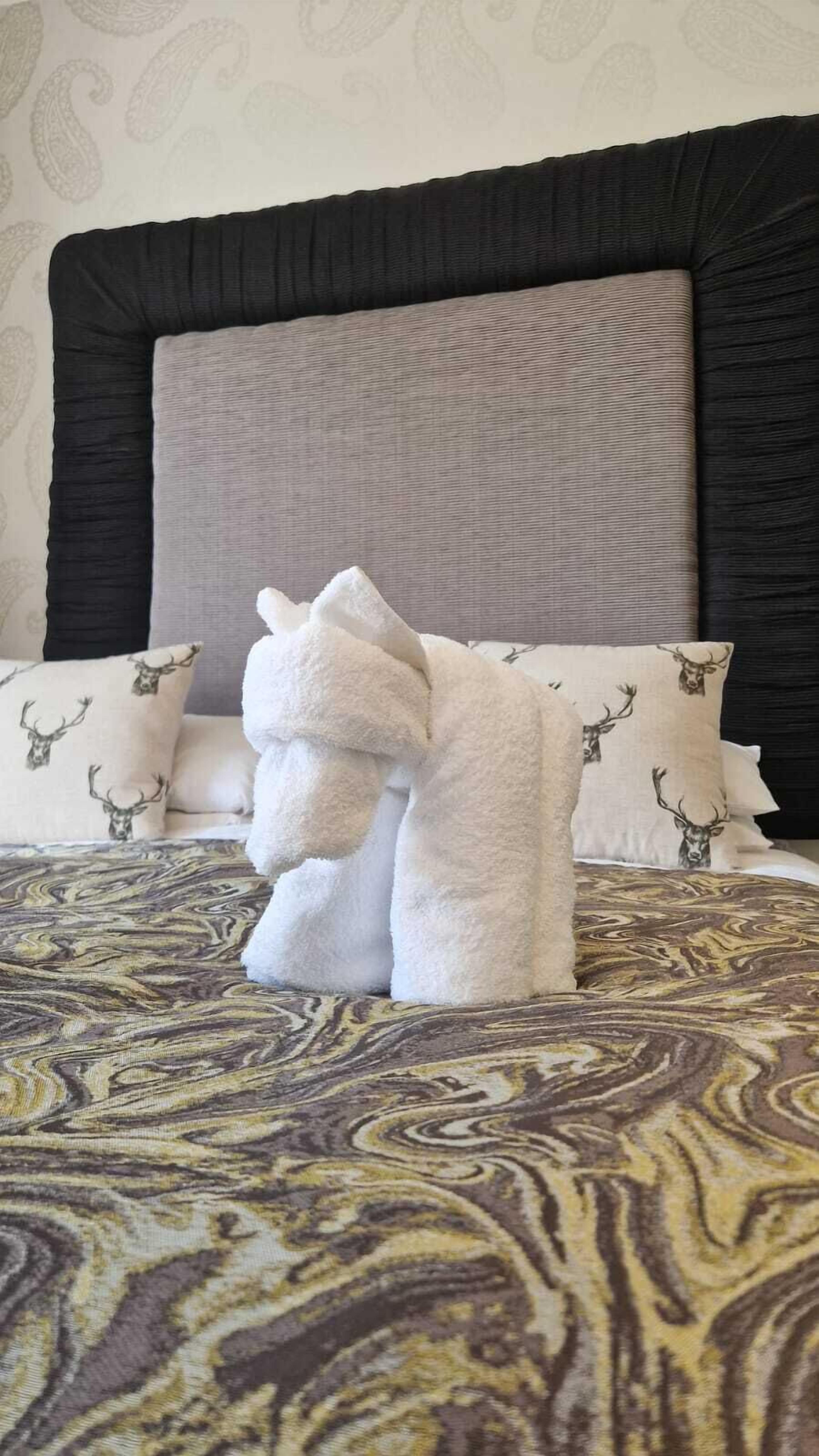 A neatly made bed with a patterned bedspread, two pillows with a deer print, and a white towel folded on the bed.