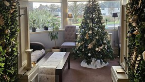 Une pièce chaleureuse avec un sapin de Noël, un banc et une vue sur l’extérieur.