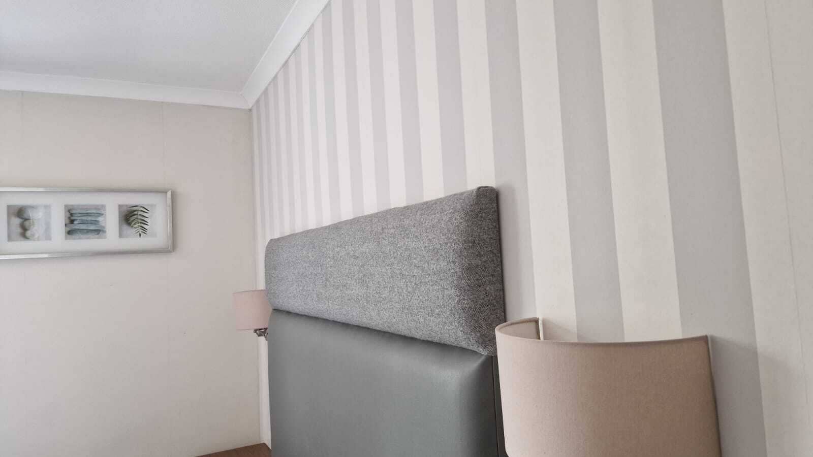 A room with a grey upholstered headboard, a bedside lamp, and a framed picture on the wall.