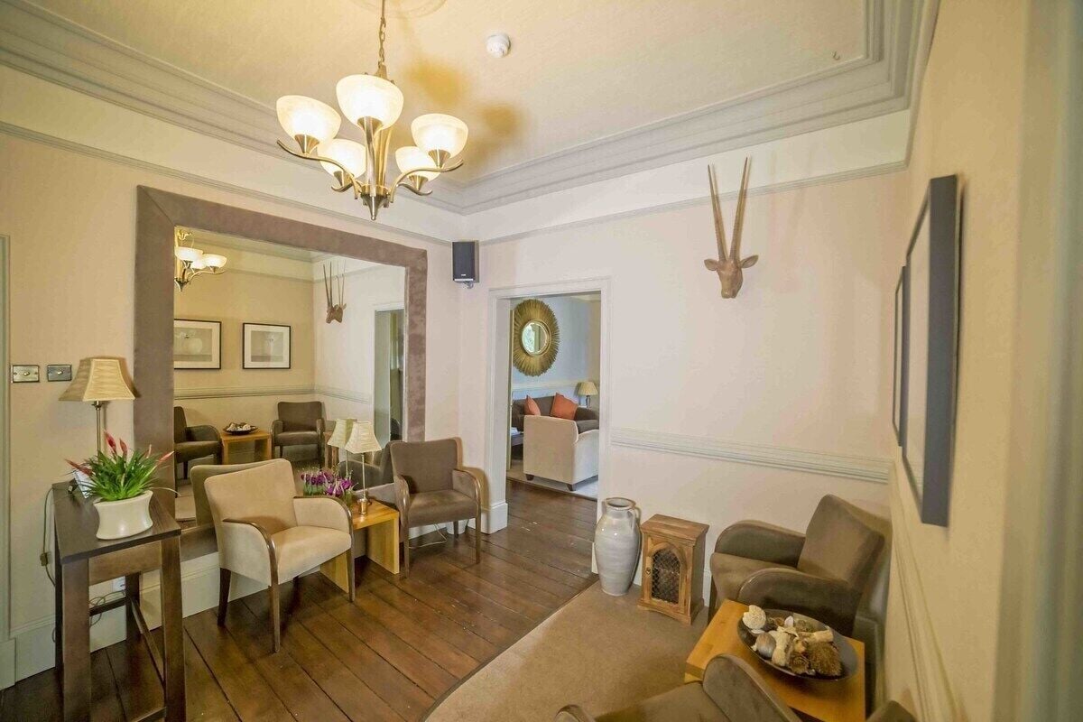 A spacious living room with a chandelier, multiple seating areas, and a large mirror.