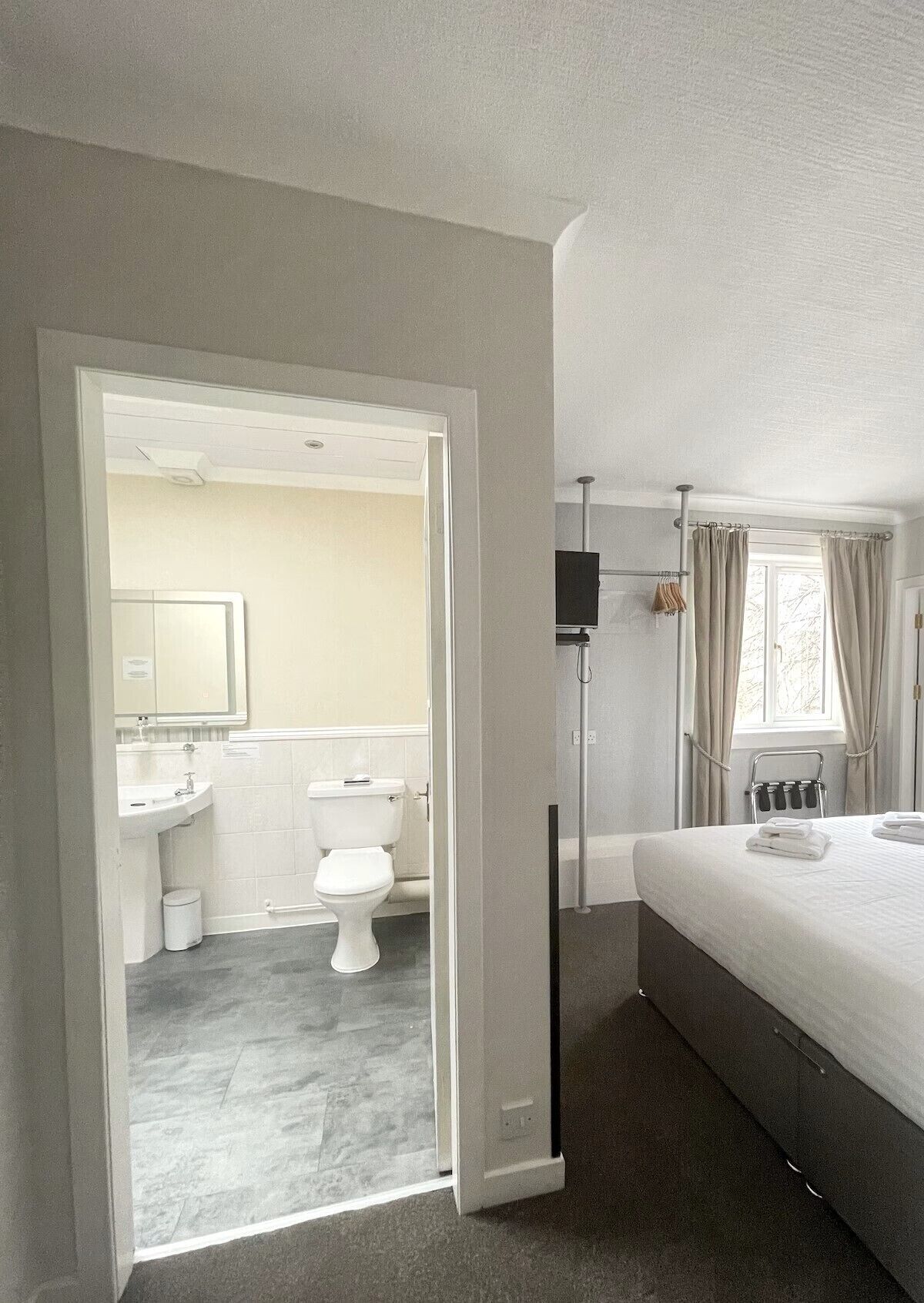 A hotel room with a bathroom, a bed, and a window with curtains.