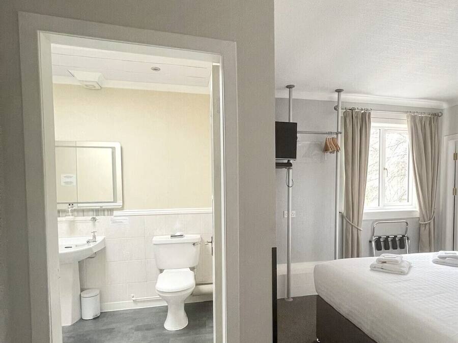 A hotel room with a bathroom, a bed, and a window with curtains.