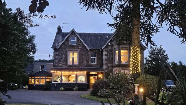 Une grande maison à deux étages, dotée d’une entrée bien éclairée et d’une allée menant à la porte d’entrée.