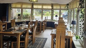 Un restaurant avec des tables et des chaises en bois, de grandes fenêtres et un plafond tendu.