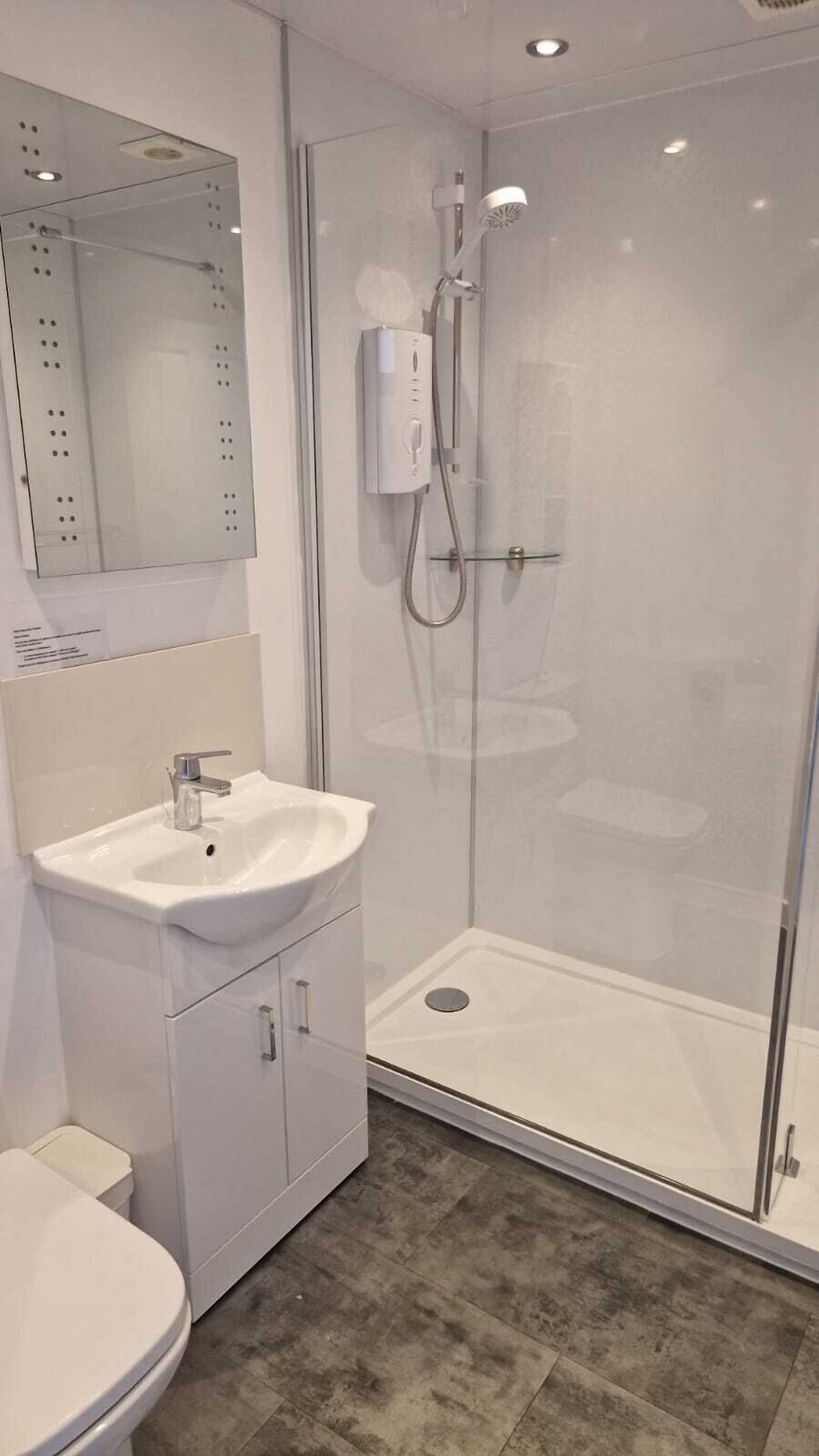 A modern bathroom with a glass-enclosed shower, a white sink, and a toilet.