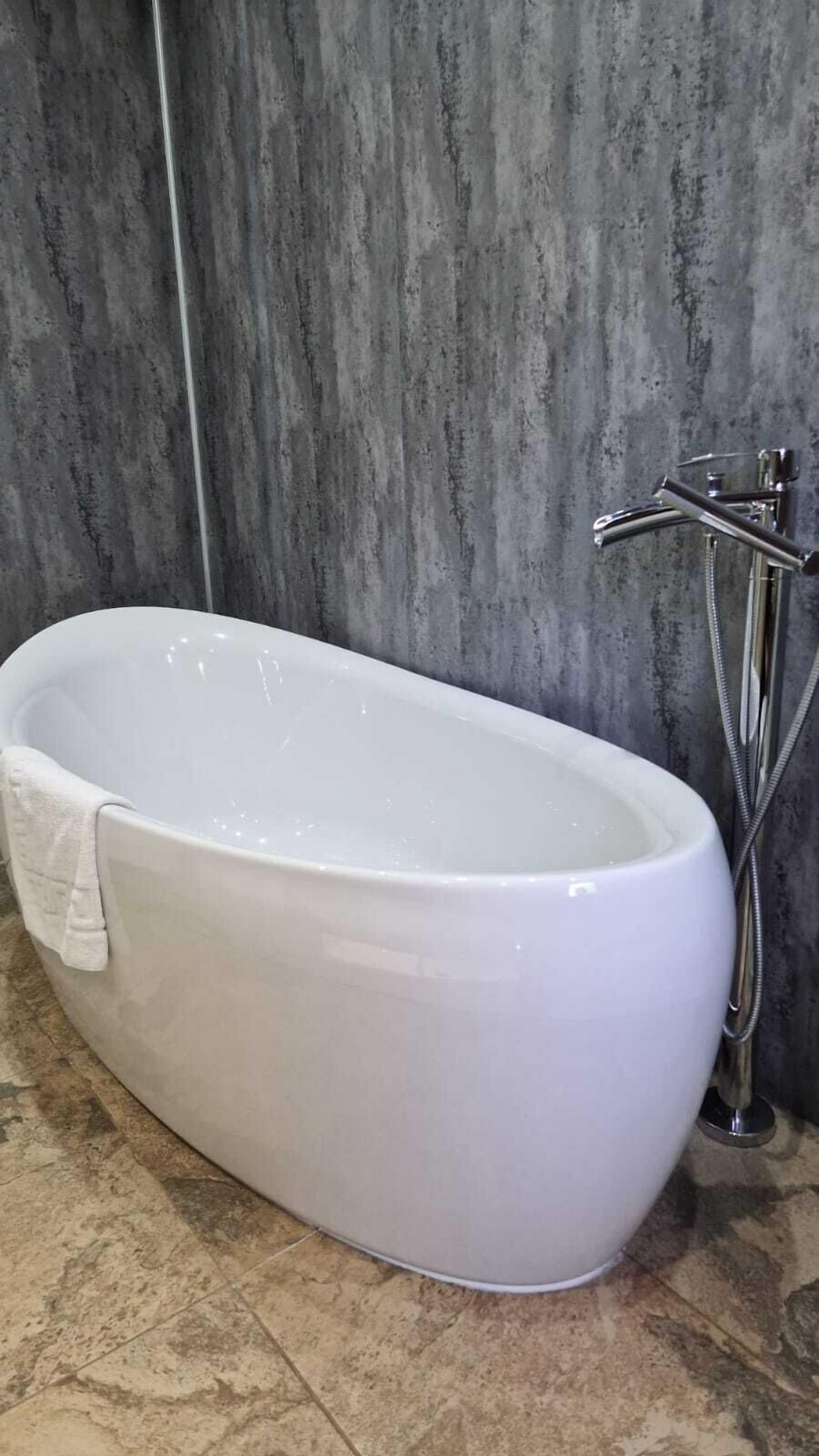 A modern bathroom with a freestanding bathtub, a chrome faucet, and a textured wall.