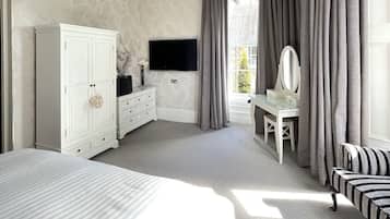 A bedroom with a bed, a dresser, a vanity with a mirror, a television, and a window with curtains.