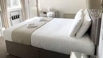 Une chambre d’hôtel avec un lit, une table de chevet, une lampe, un radiateur, une fenêtre avec des rideaux et un tableau encadré au mur.